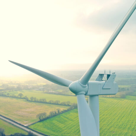 Nahaufnahme einer Windkraftanlage mit landwirtschaftlichen Flächen im Hintergrund